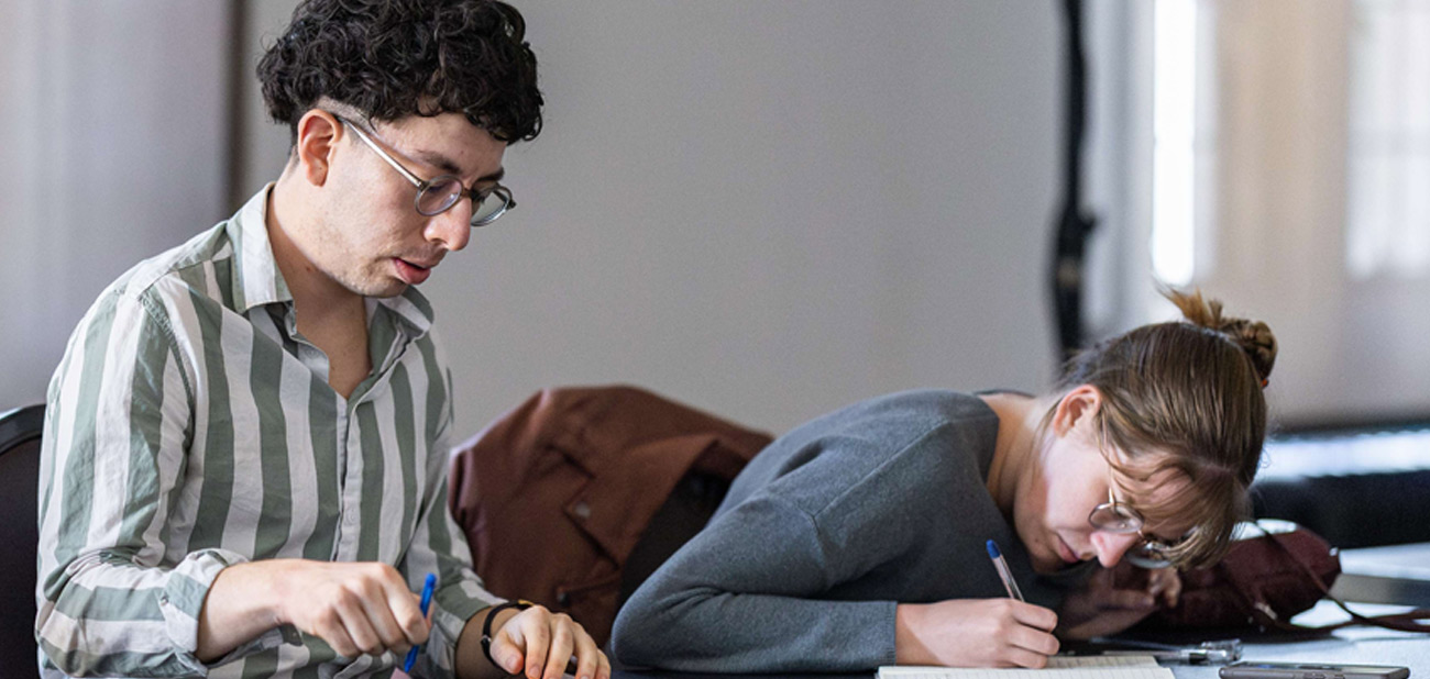 Two students writing notes during the World Universities' Debating Championship 2025