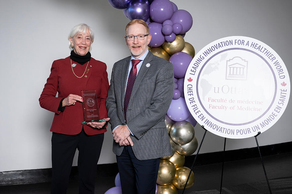 2 people pose together, with one holding an award