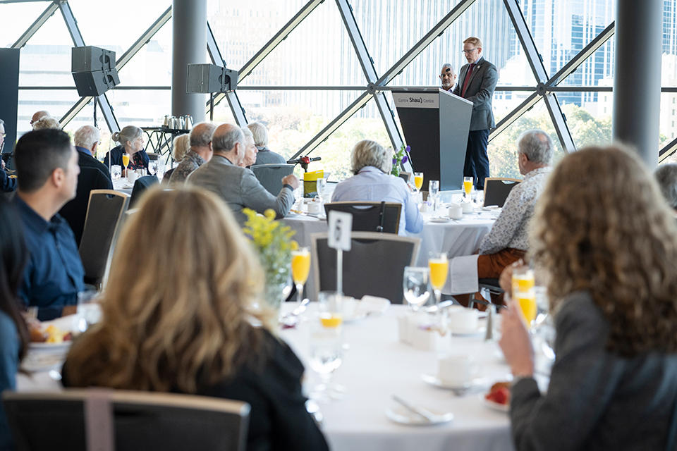 a group of people eating a meal and listening to a person speak at a podium