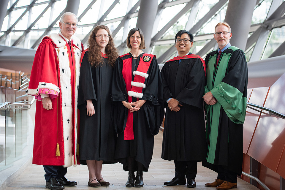 Five people pose in graduation ceremonial attire