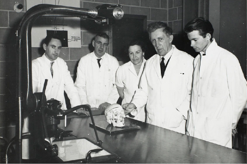 S. Bedok, Charles Marcotte, Mme Victor Linis, Martin Fokkena, standing in front of a lab table with a human skull on it.