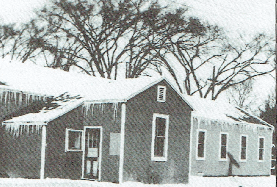 A barracks building, with snow on the roof and icicles hanging from the eaves, stands on snow-covered ground.