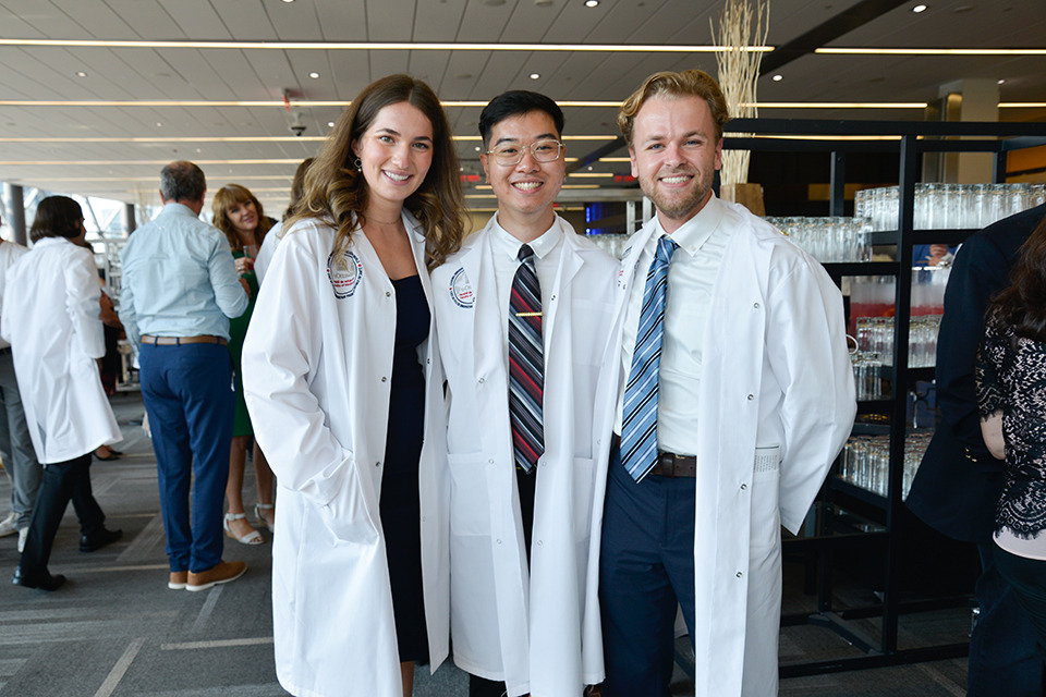 Three medical learners pose wearing their white coats.