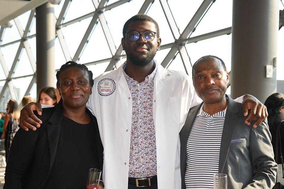 A medical learner in his white coat poses with his parents.