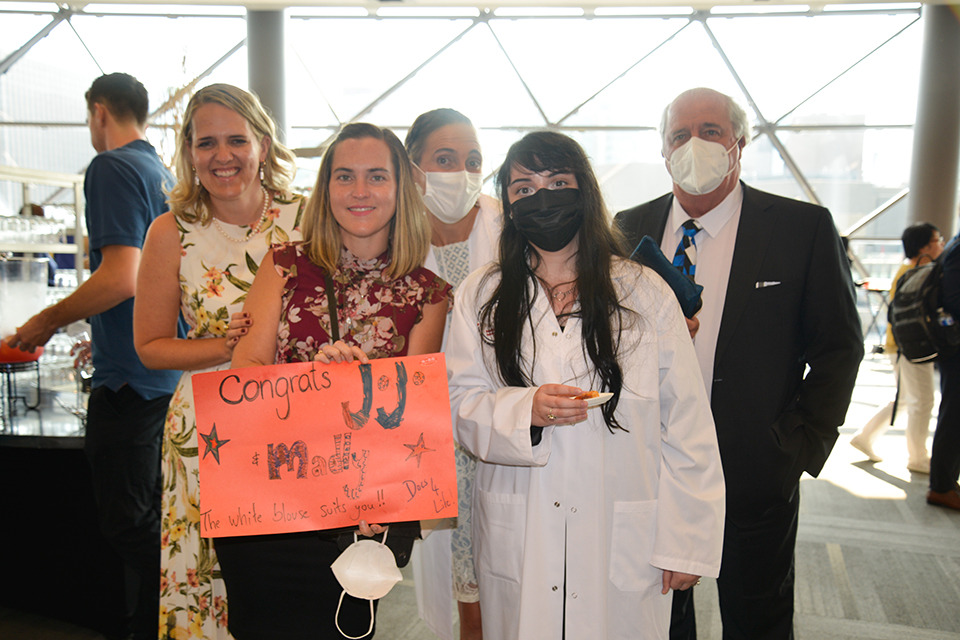 Two medical learners in their white coats poses with their parents.