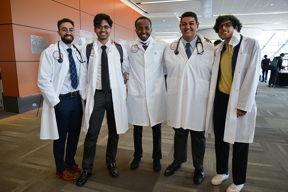 Five medical learners pose wearing their white coats.