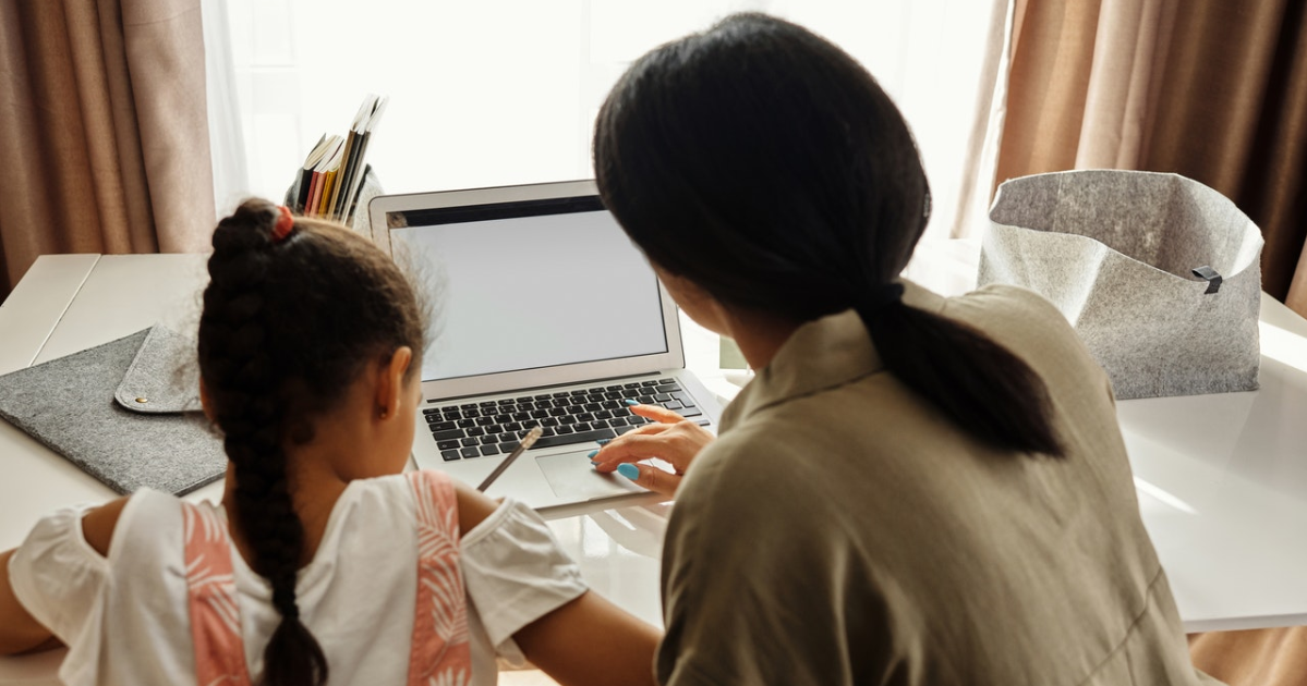A young girl doing homework in front of the computer with an adult