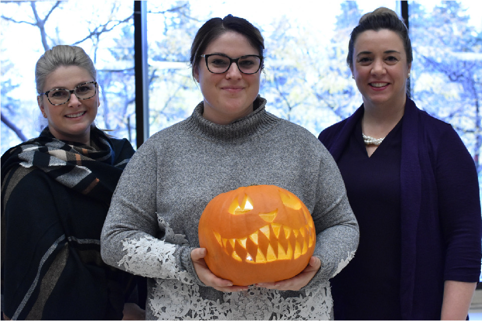 Josée Lortie and Michelle Émard stand on either side of Jenn Therrien, who holds a grinning jack-o’-lantern.
