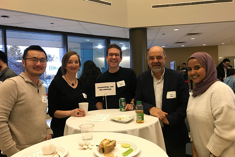 A photo of students and faculty standing at a cocktail table.