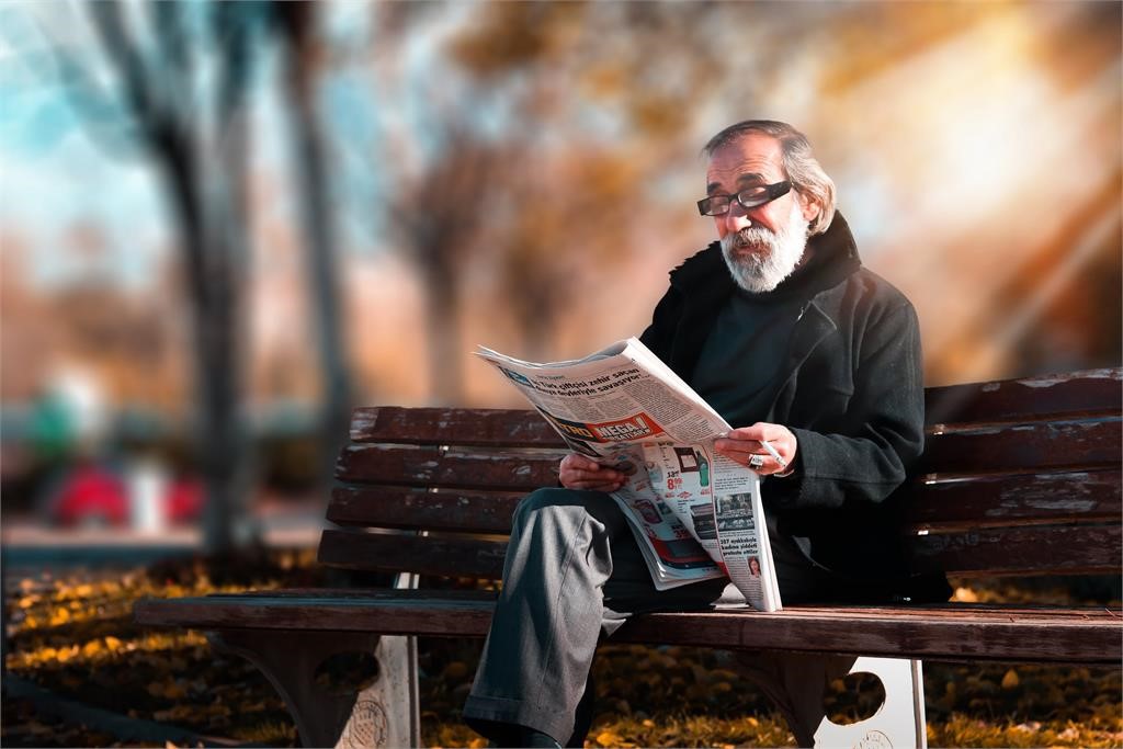 Older man sitting on a bench reading a newspaper