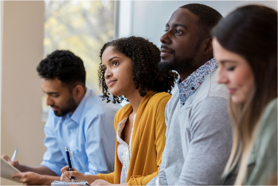 Four university students of different ethnic backgrounds sit in a row, with a window behind them.
