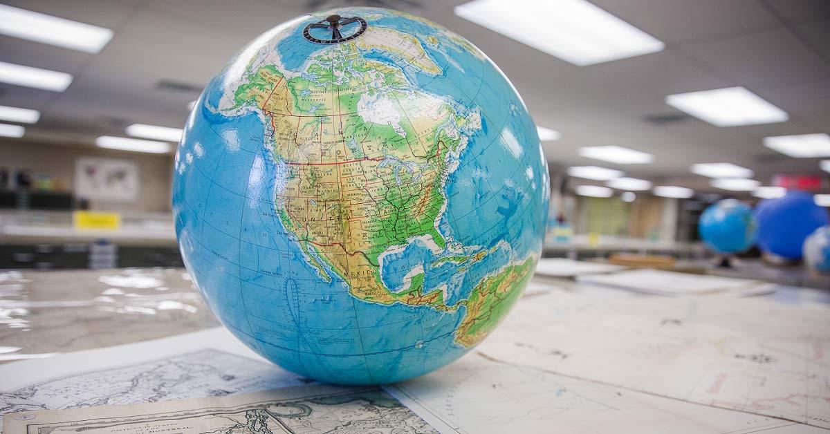 Close-up of a globe tilted toward North America, with a map library in the background.