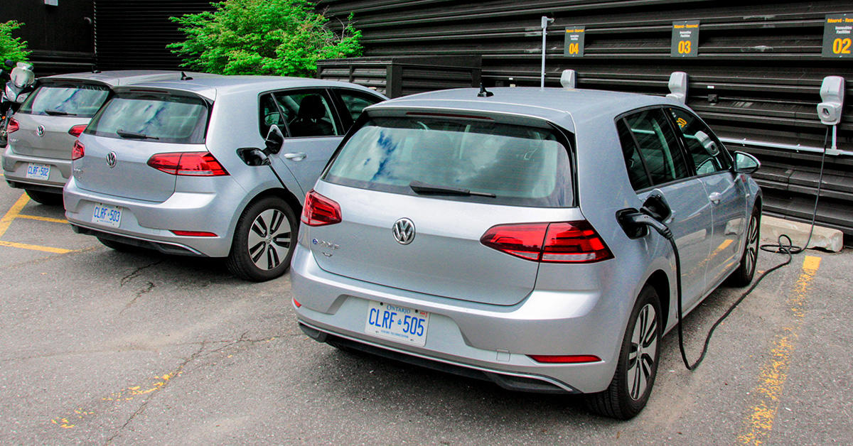 three electric volkswagens parked in a row and plugged in to chargers